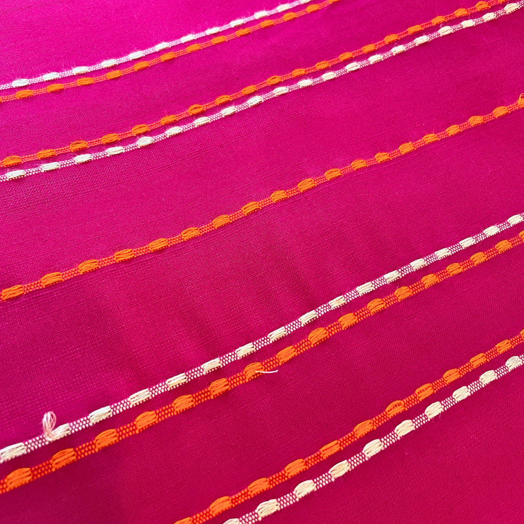 Close-up of pink fabric with orange and white thread patterns